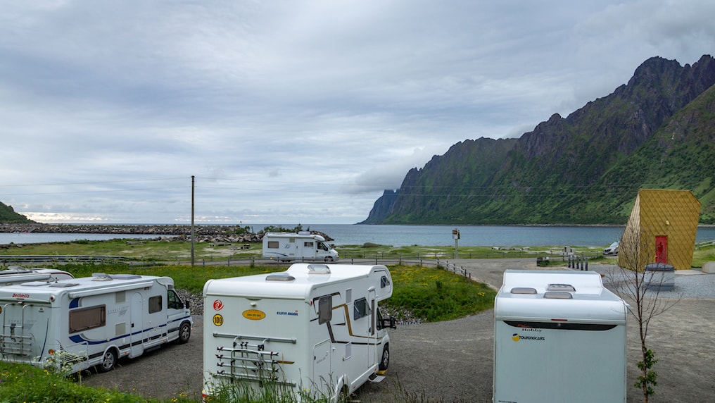 Three motorhomes parked in front of a toilet building. 