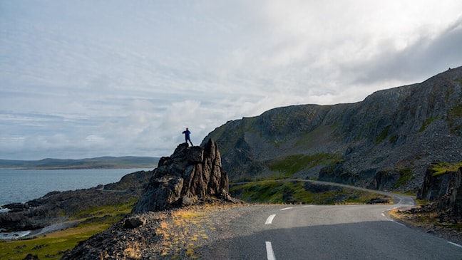 Person taking a picture along the road in a rugged rocky landscape.