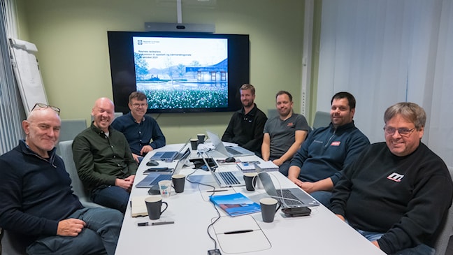 Sju menn sitter rundt et bord. 