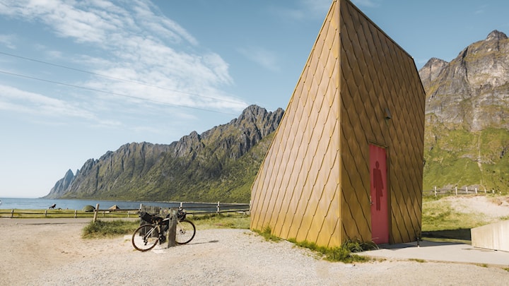 WC-Anlage an einem wunderschönen Sandstrand. Die Anlage ist ein dreieckiges Gebäude und hat eine vergoldete Außenfläche. 