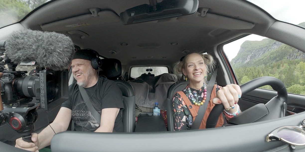 Mann og dame sitter i en bil og kjører. 