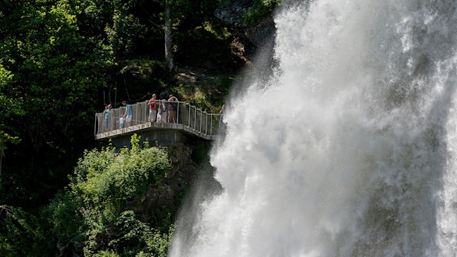 Brusende foss foran plattform med mange mennesker.