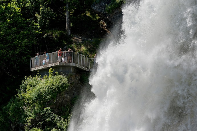 Brusende foss foran plattform med mange mennesker.
