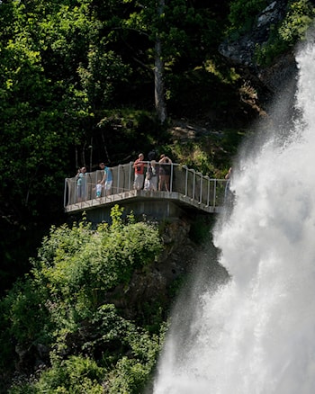 Brusende foss foran plattform med mange mennesker.