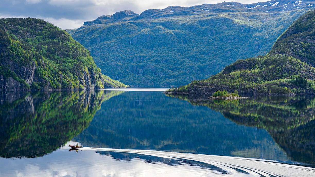 Blikk stille vann, grønnkledde bergvegger helt ned i fjorden.