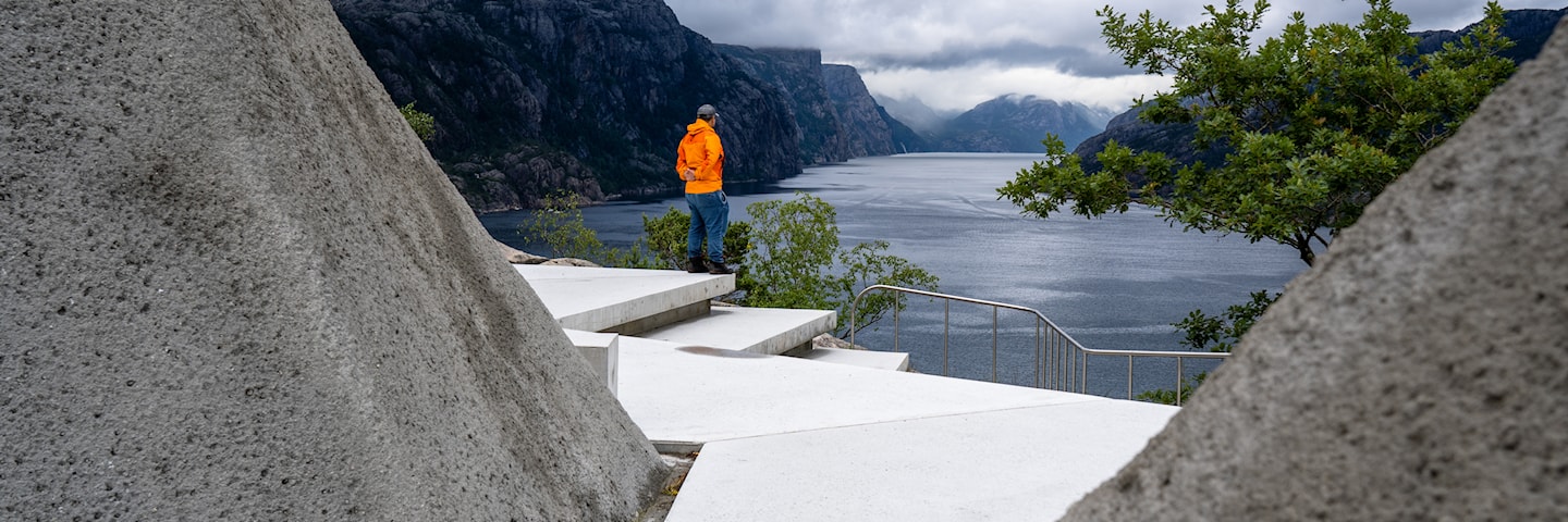 Betongsti går i en kløft av skråninger belagt med betong. Terrenget åpner seg opp med utsikt utover fjorden.