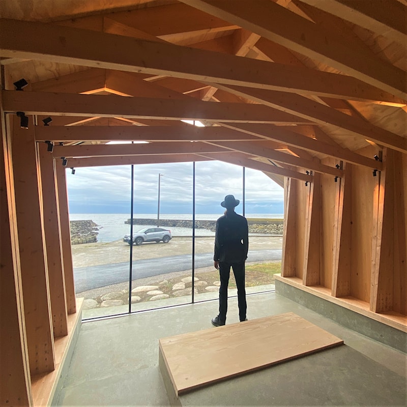 Rullesteinsstrand med skipsvrak i det fjerne.